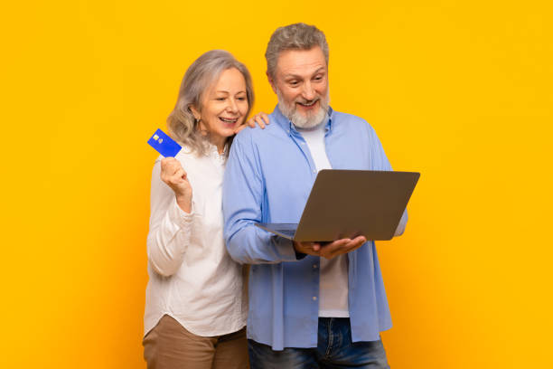 istock senior couple browsing website on laptop holding credit card, studio 2164478062