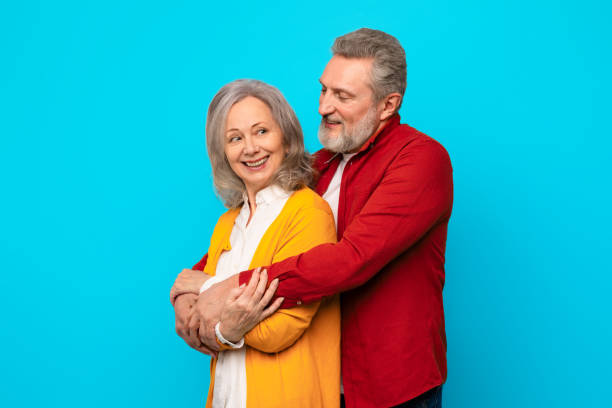 istock Happy loving senior couple embracing with affection against blue backdrop 2164478083