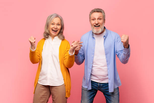 istock Excited mature spouses celebrating with yes gestures over pink backdrop 2164478087