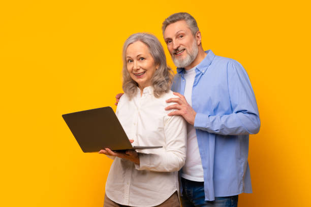 istock Smiling elderly husband and wife standing with computer, yellow studio 2164478108