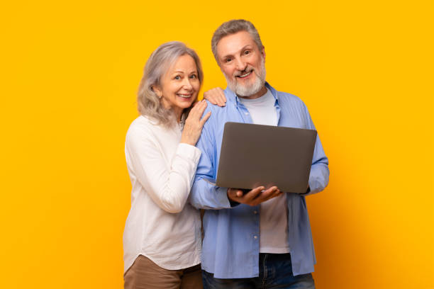 istock Senior couple enjoying online browsing together on modern laptop, studio 2164478122