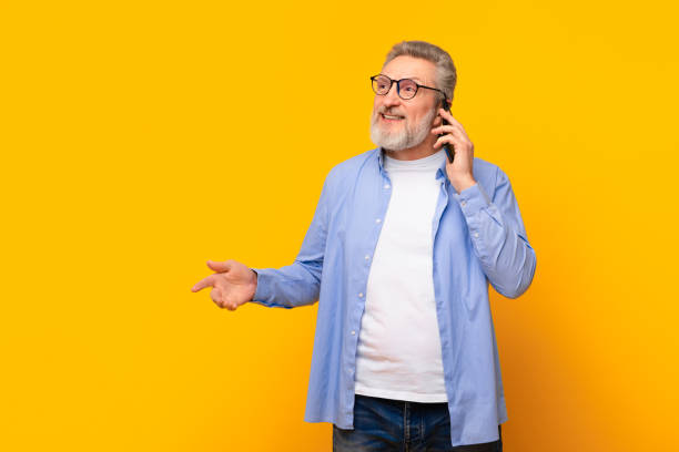 istock Cheerful senior man talking on cell phone on yellow background 2164478128