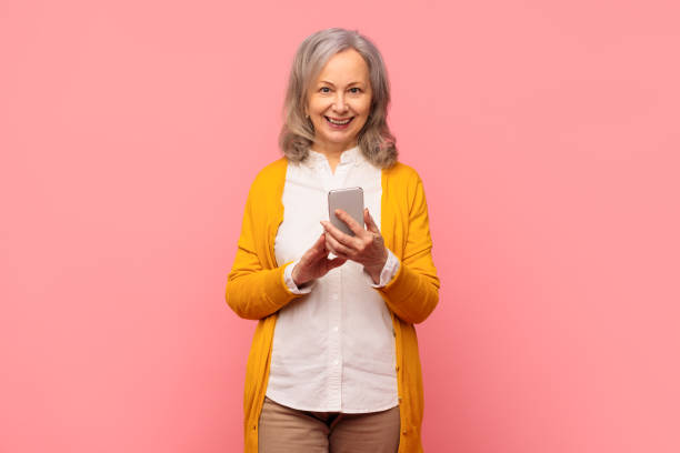 istock Cheerful mature gray haired woman texting via cell phone, studio 2164478168
