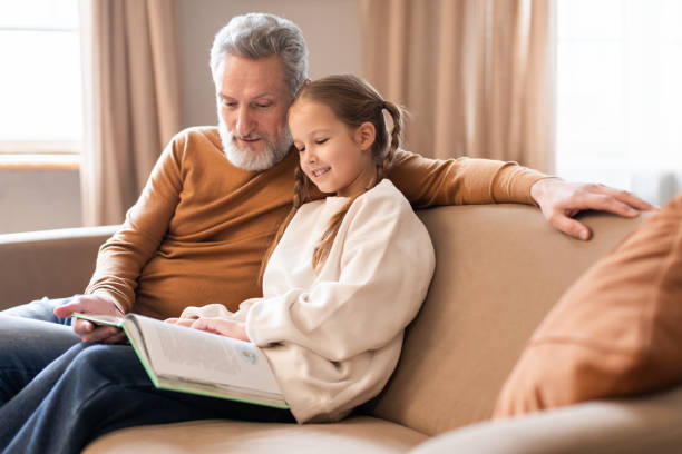 istock Man and Little Girl Reading Book on Couch 2164480946