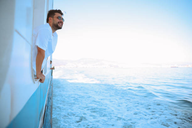Young tourist man moving around Turkey, using a ferry boat. He is wearing sunglasses, watching the Izmir panorama around her.