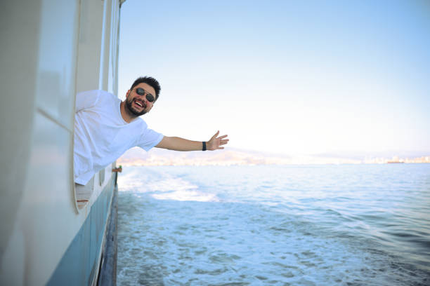 Young tourist man moving around Turkey, using a ferry boat. He is wearing sunglasses, watching the Izmir panorama around her.