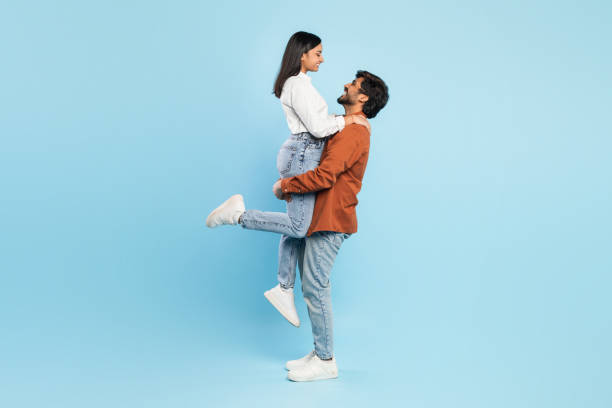 istock Man lifting woman on blue background in joyful pose 2164484709