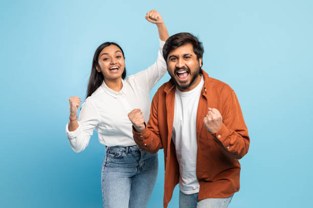 istock Couple cheering joyfully with raised fists on blue 2164484724