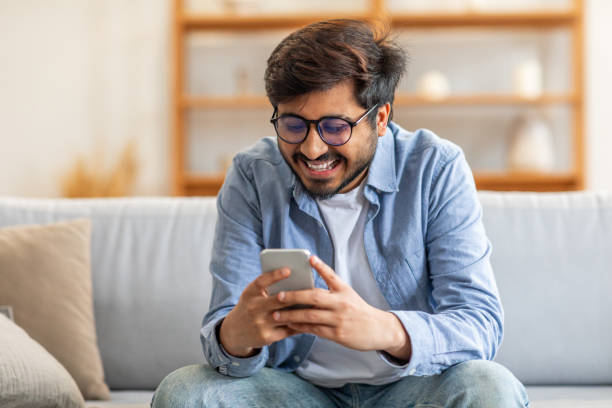 istock Man Sitting on Couch Looking at Cell Phone 2164487294