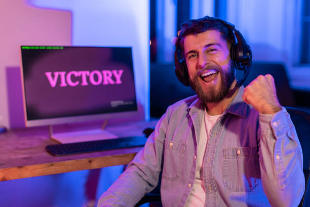 istock Gamer exuberantly fist pumps with 'VICTORY' on desktop screen 2164489427