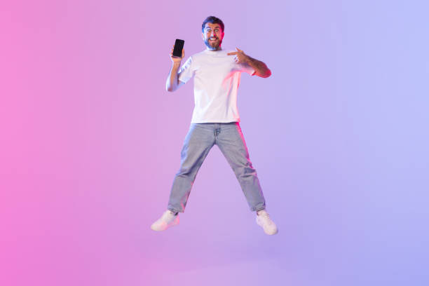 istock Excited Young Man Jumping With Smartphone on Vibrant Background 2164492173