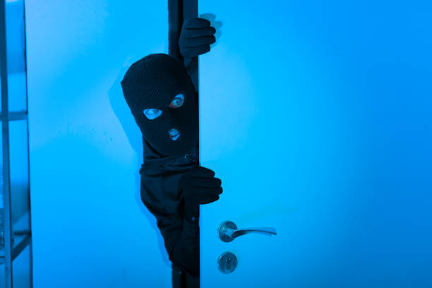 istock Burglar peeking through door in blue light 2164493492
