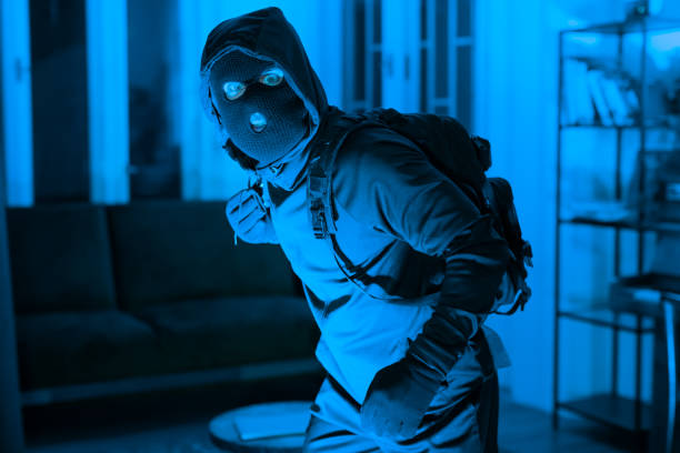 istock Burglar in mask sneaking inside a house 2164493530