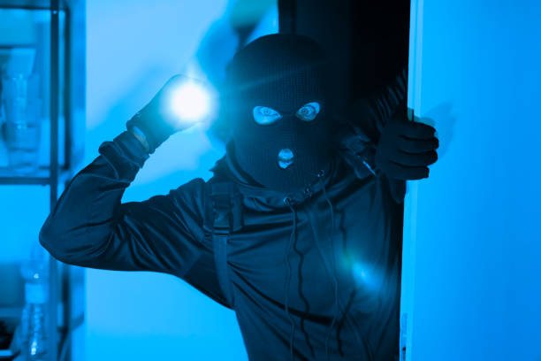 istock Burglar with flashlight illuminating his face in dark room 2164493551