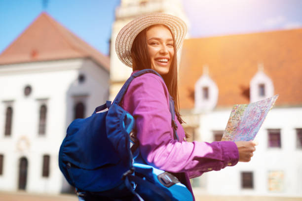 istock Smiling young woman holding map and waving 2164496037