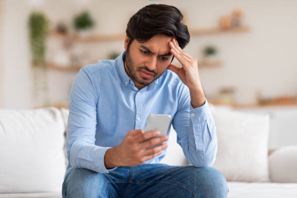 istock Worried Man Checking Phone While Sitting on Couch 2164497694
