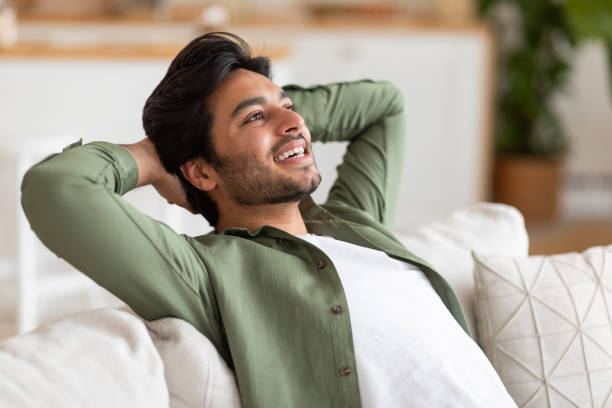 istock Relaxed Man Leaning Back On Couch In Green Shirt, Smiling 2164497706