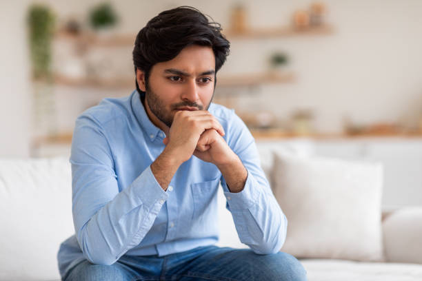 istock Pensive Young Man Sitting on a Couch Indoors 2164497709