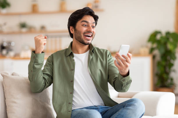 istock Excited Young Man Celebrating Success on Smartphone 2164497723