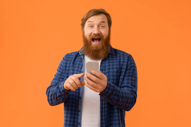 istock Red haired businessman expresses surprise using app on smartphone, studio 2164497895