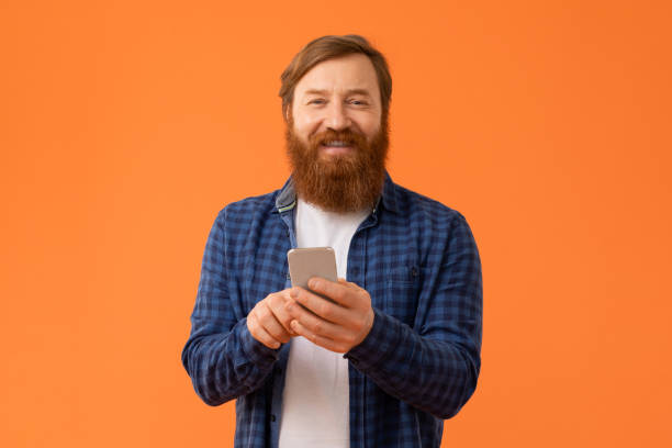 istock Man with red hair and beard engages with smartphone, studio 2164497896