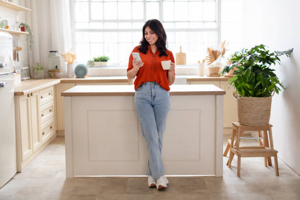 istock Woman with coffee and phone in a bright kitchen 2164499384