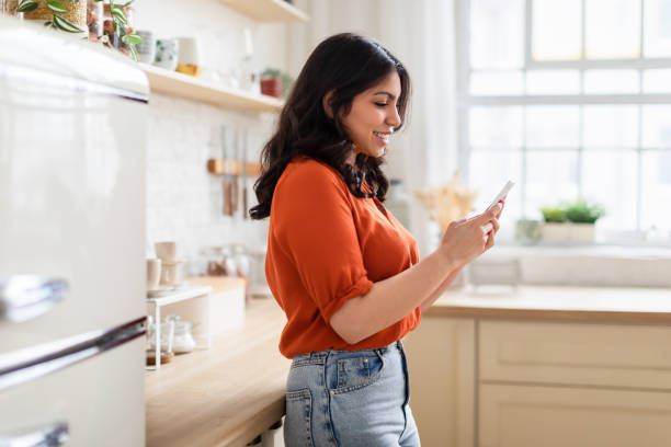 istock Woman browsing phone in a cozy kitchen 2164499388