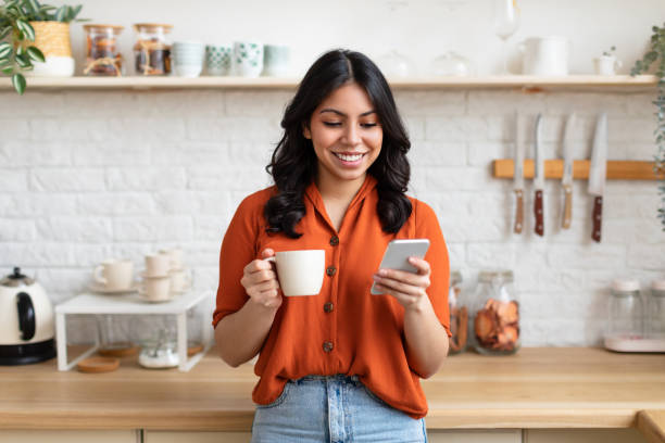 istock Cheerful woman using phone with coffee at home 2164499429