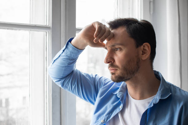 istock Man Looking Out Window With Hand on Head 2164502173