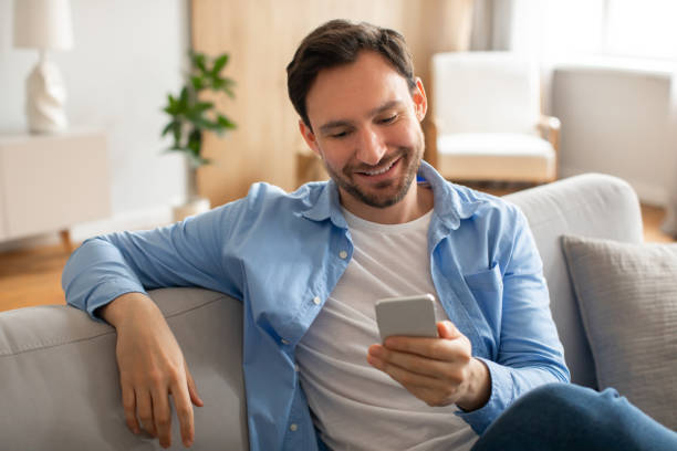 istock Man Sitting on Couch Looking at Cell Phone 2164502174