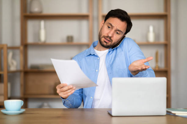 istock Confused Man With Document in Hand Working on a Laptop 2164502198