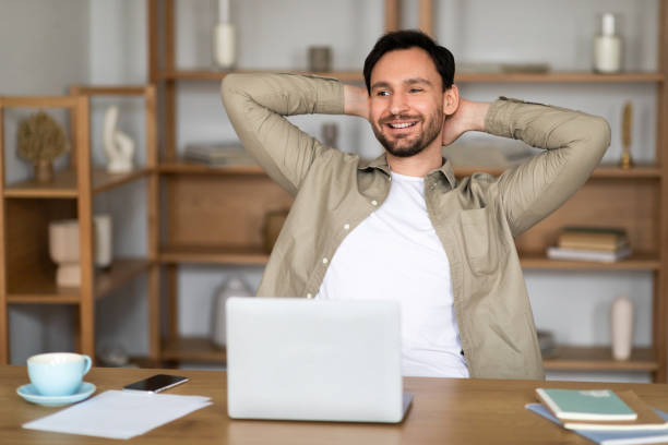 istock Young Man Relaxing at His Desk With Laptop and Coffee 2164502199