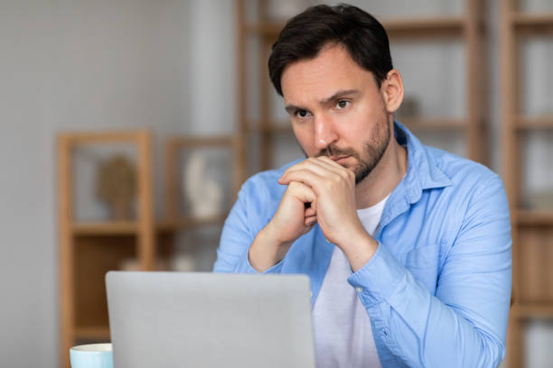 istock Man Sitting in Front of Laptop With Hand on Chin 2164502205