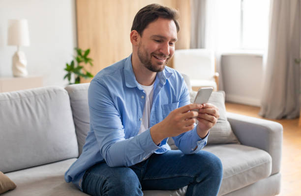 istock Man Sitting on Couch Looking at Phone, Chatting 2164502225