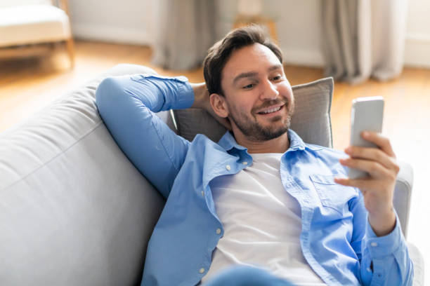 istock Positive Man Sitting on Couch Looking at Phone 2164502435