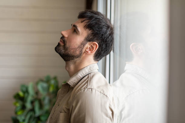 istock Man Standing in Front of Window, Feeling Down 2164504722