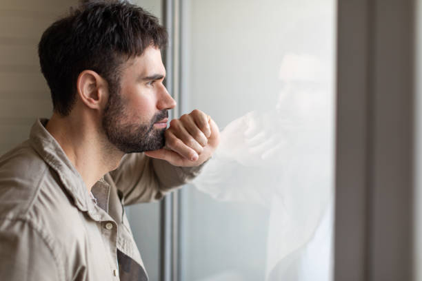 istock Man Looking Out a Window With Hand on Face 2164504726