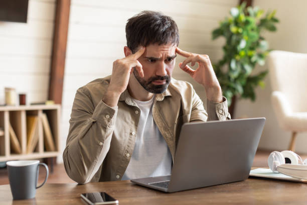 istock Concerned Man Frowning While Working on Laptop in Home Office 2164504738