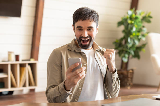 istock Ecstatic Young Man Celebrating Success With Smartphone Indoors During Daytime 2164504760