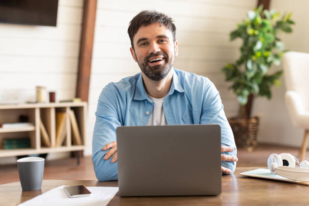 istock Man Sitting in Front of Laptop Computer, Smiling at Camera 2164504772