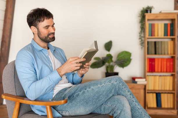 istock Man Sitting in Chair Reading Book at Home 2164504775