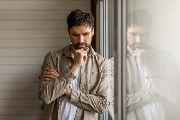 istock Pensive Man Leaning Against Window Reflecting on a Cloudy Afternoon 2164504812