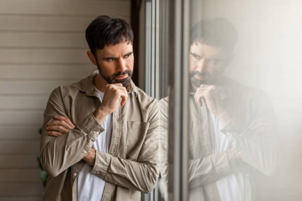 istock Pensive Man With Beard Standing Near Window Reflecting on Thoughts 2164504821