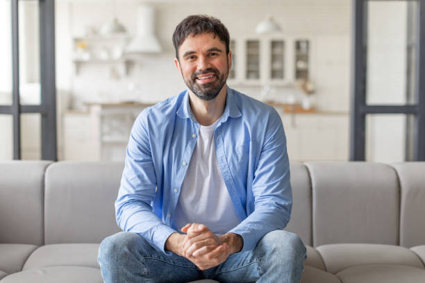 istock Smiling Man Sitting on Couch in a Modern Living Room 2164505603