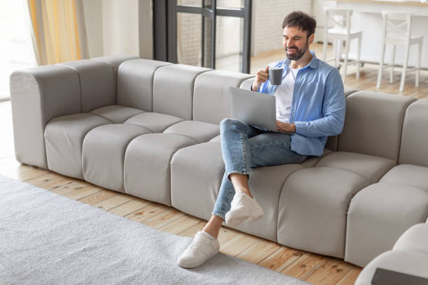 istock Man Relaxing On A Modular Sofa With Laptop And Coffee 2164505605