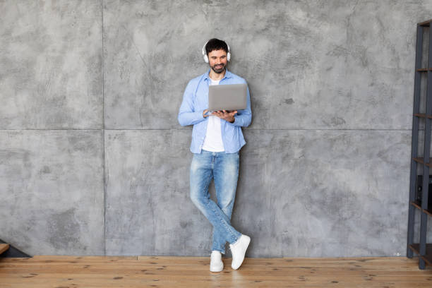 istock Man Using Laptop Against Concrete Wall With Headphones 2164505613