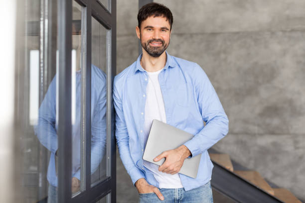 istock Smiling Man Holding Laptop While Standing in an Office 2164505622