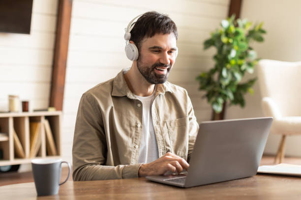istock Man Sitting at Table With Laptop and Headphones On, Working 2164505640