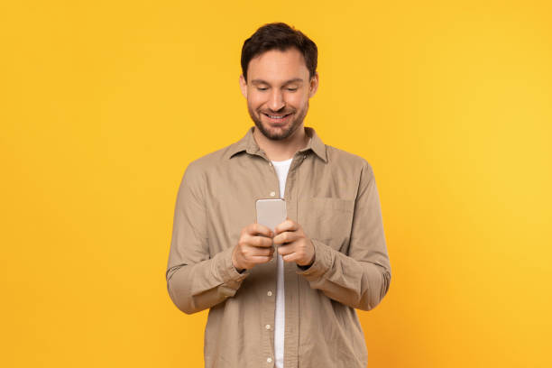 istock Man Standing in Front of Yellow Wall With Cell Phone 2164506529