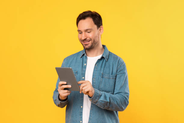 istock Man in Blue Shirt Looking at Tablet, Yellow Background 2164506585